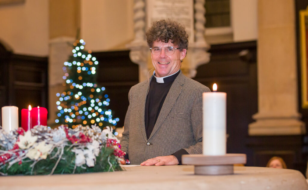 This is Reverend Stephen Baxter at the St Stephens Church at the Success Charity Carol Concert. He is standing smiling.